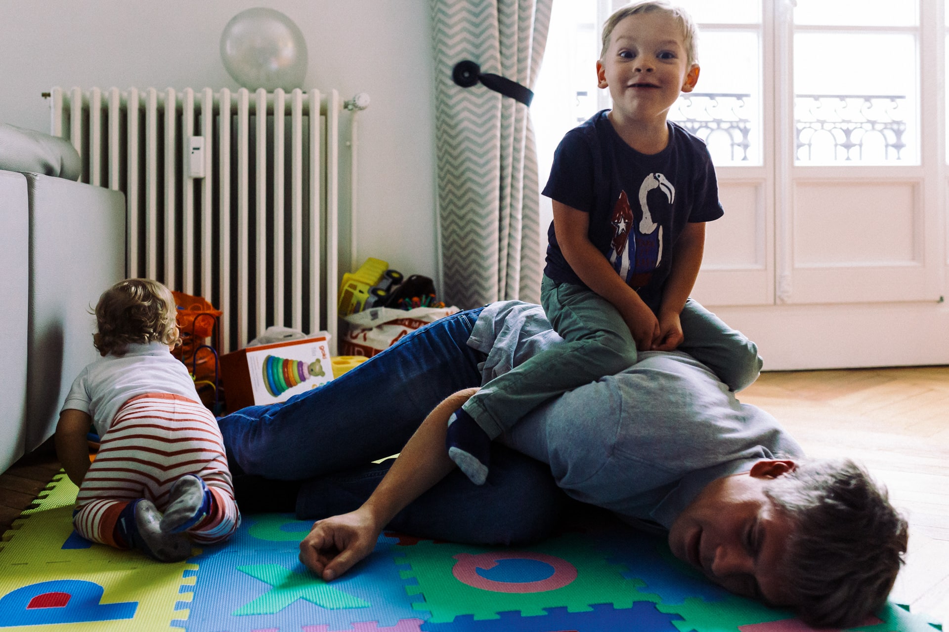 Ernestine et sa famille - wedding and life photographer - 1920-1 ‣ Photographe de famille à l'approche documentaire pour vos évènements ou votre vie quotidienne, à Paris et dans toute la France petit garçon qui joue a escalader sur son son papa et son frère à coté. Reportage de famille à Neuilly (92) par Ernestine et sa famille