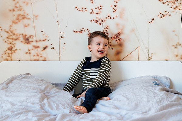 Garçon qui rie dans le lit des parents. Reportage de vie quotidienne à domicile à Issy les Moulineaux.