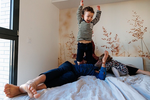 Petit garçon saute au dessus de ses parents sur le lit. Reportage de vie quotidienne à domicile à Issy les Moulineaux.